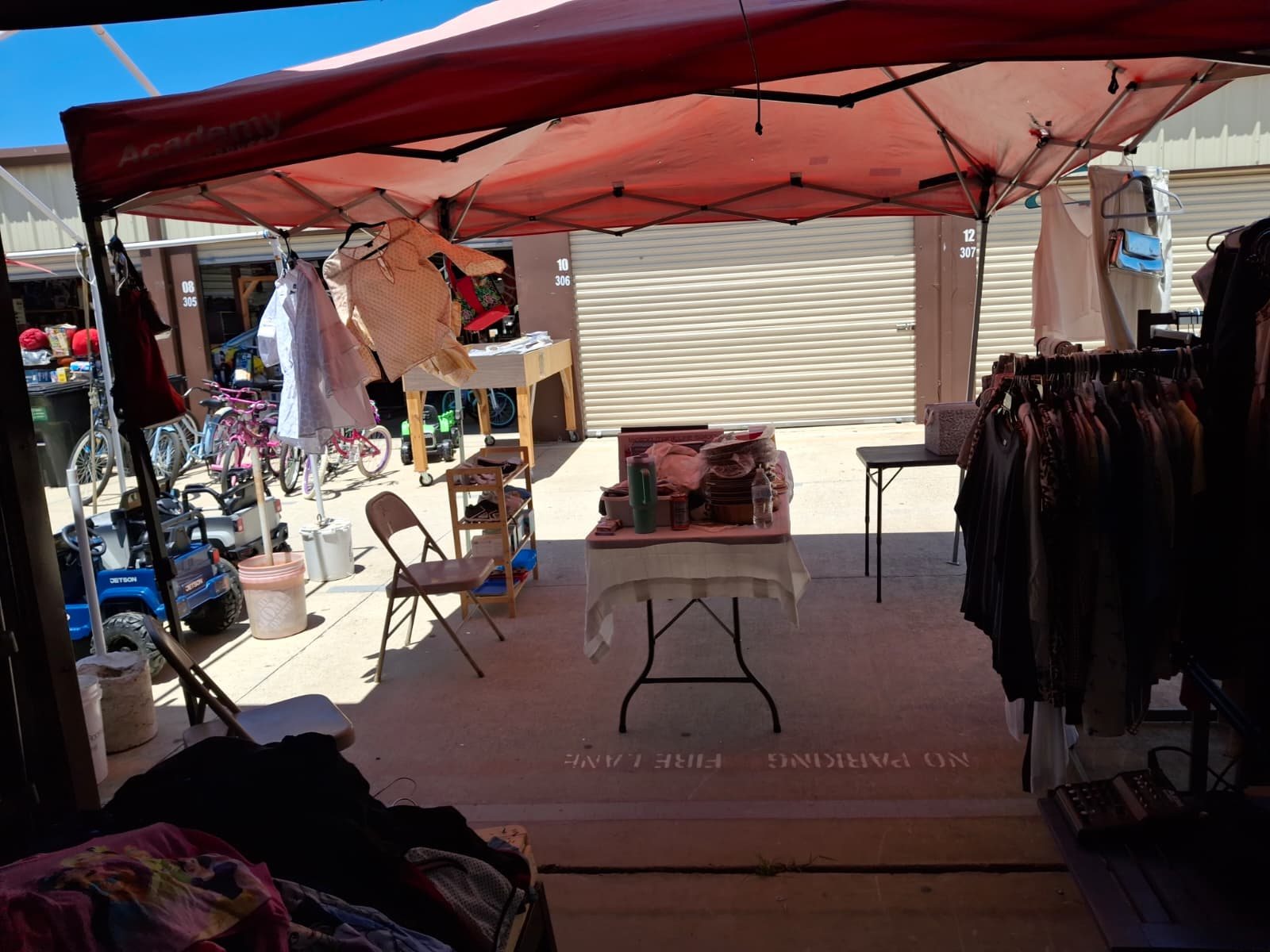 Outdoor market booth with clothing racks, bikes and household items